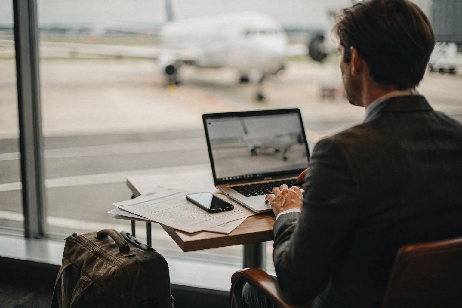 A consultant working on a laptop at an airport lounge window