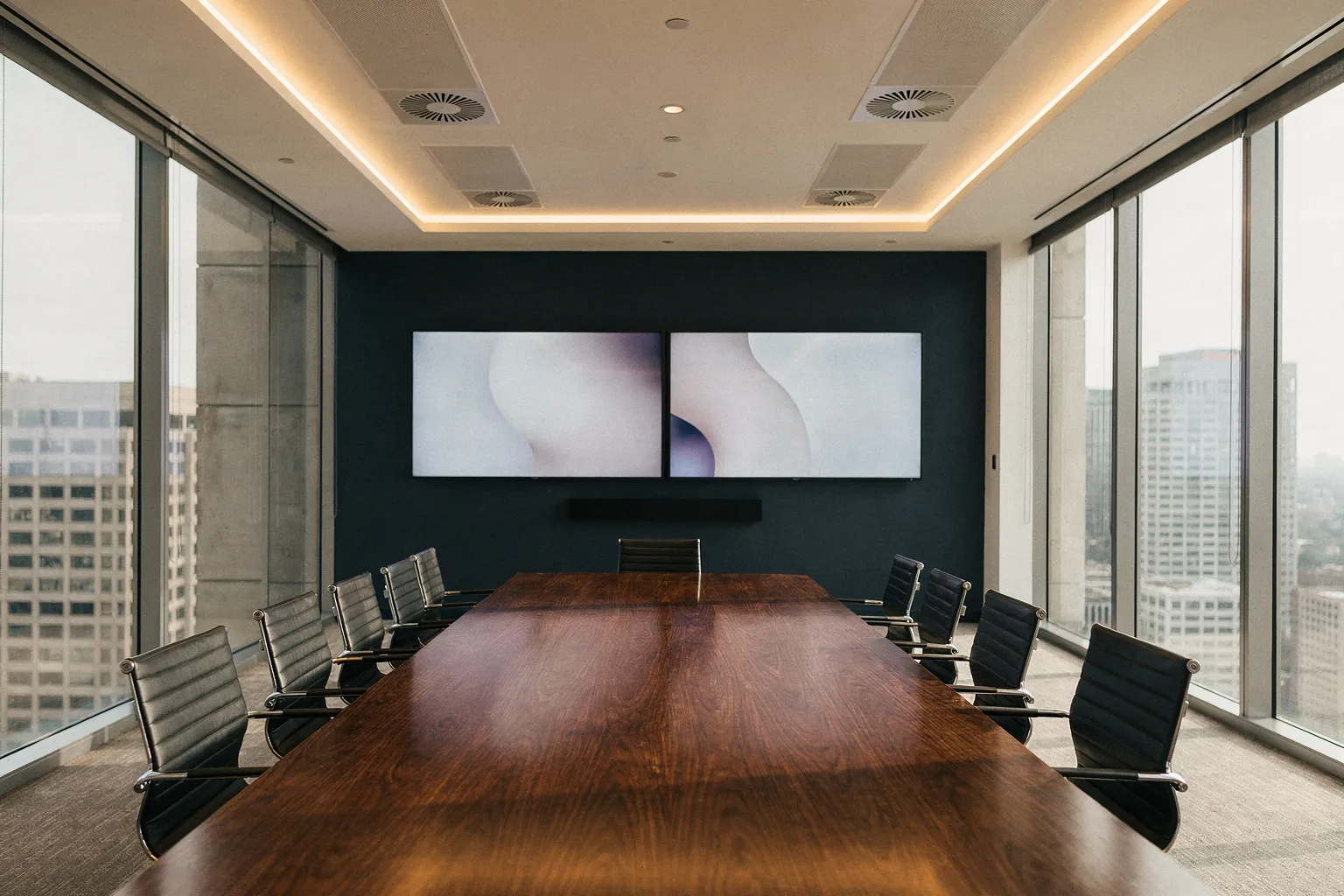 Boardroom with a long walnut table, dual wall displays and a video bar